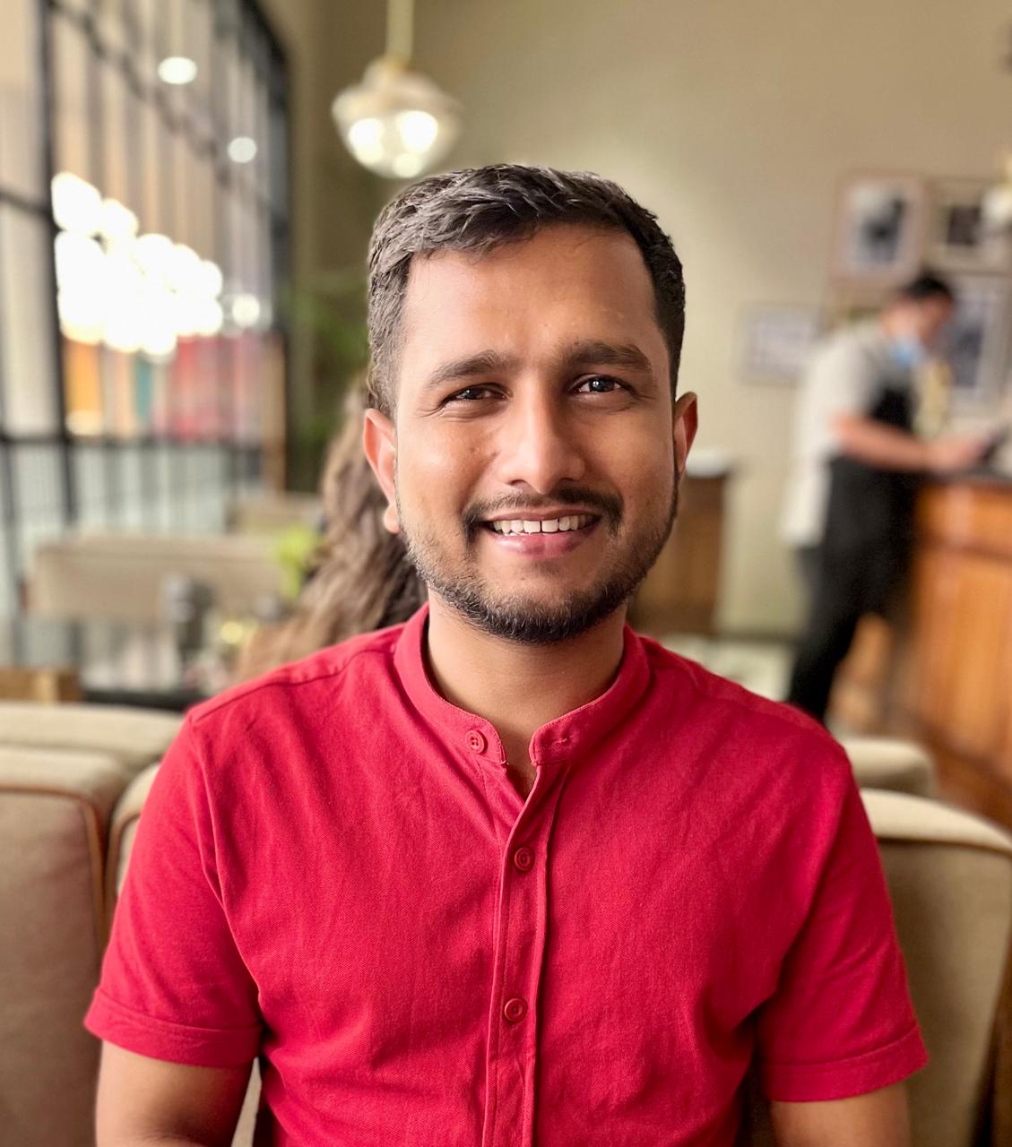 Samuel Dias, smiling, in a red shirt in a cafe