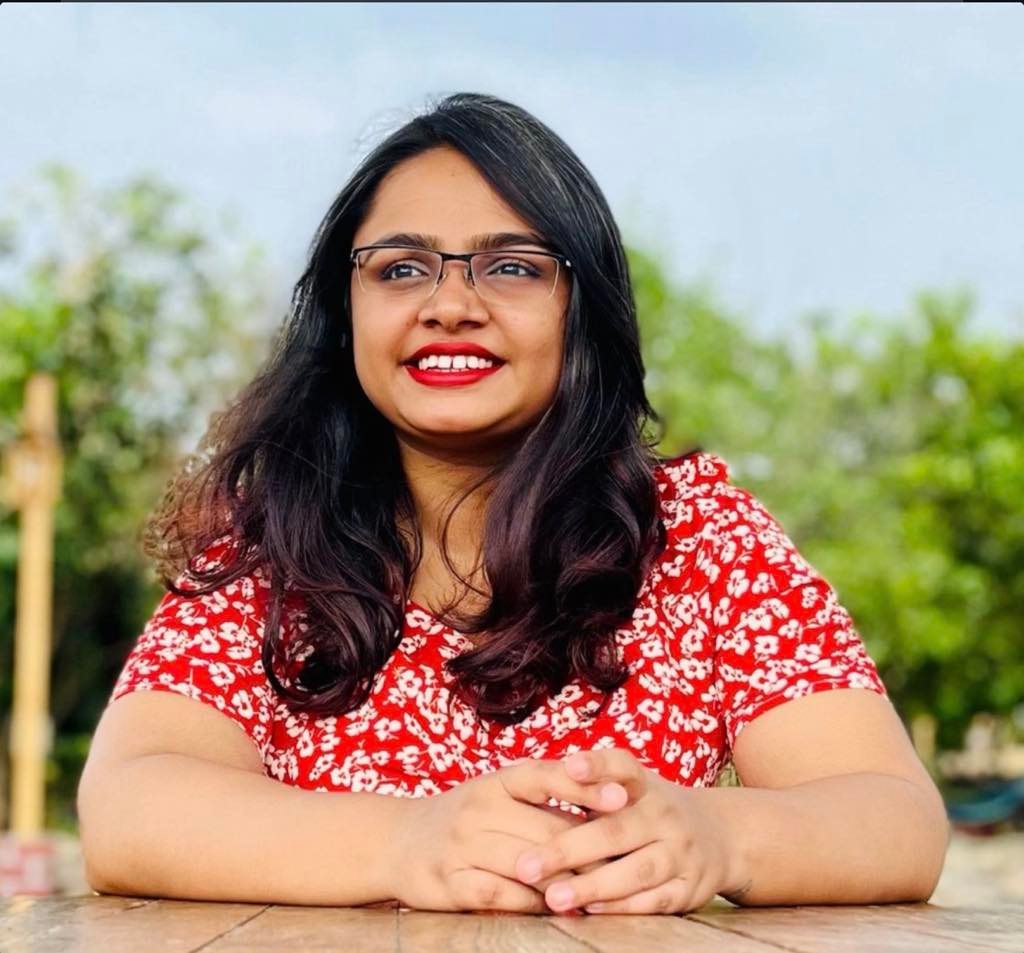 Shrawani Pawar, smiling, seated at a wooden table outdoors